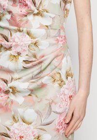 Zbliżenie na kwiecistą sukienkę z dużymi białymi i różowymi kwiatami, zielonymi liśćmi oraz prawą ręką osoby spoczywającą obok.
