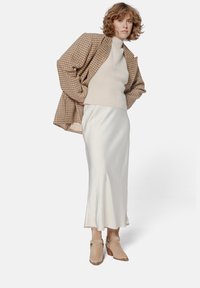 Brown plaid oversized jacket over a beige knit sweater, paired with a white satin slip skirt and beige ankle boots with a strap detail.