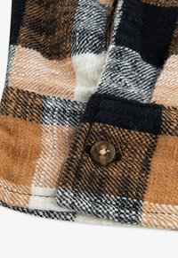 Tessuto flanella a quadri marrone e nero con accenti bianchi. Include un bottone marrone testurizzato e una trama visibile.