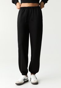 Pantaloni de jogging negri cu talie elastică, șnur ajustabil și manșete înguste. Asortați cu adidași albi și gri.
