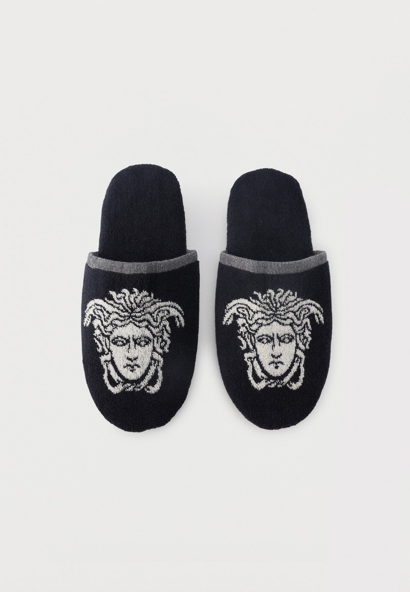 Black slip-on slippers with gray trim, each featuring a white Medusa head design on the front.