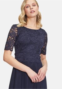 Námornícká modrá šaty s kvetinovou čipkovou blúzkou a krátkymi rukávmi, hladká splývavá sukňa a detaily so zubatým čipkovým lemovaním.