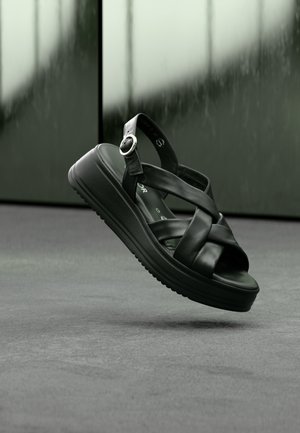 Schwarze Lederkeilabsatz-Sandalen mit Kreuzriemen und einer runden Metallschnalle. Strukturierte Sohle für besseren Halt, mit einem glatten Innenfutter.