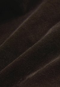 Ruskea korduroykangas, jossa on tupsutettu rakenne, näkyvissä poimutetut linjat ja hienovarainen kiilto, taitettuna näyttämään syvyyttä ja ulottuvuutta.