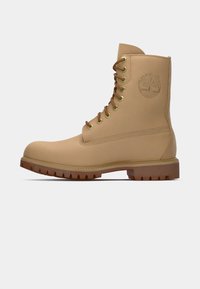 Botte lacée beige avec une tige lisse, bout rond, semelle en caoutchouc et motif de traction marron contrastant, présentant un logo embossé sur le côté.