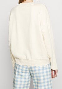 Felpa oversize color crema con collo rotondo e orlo a costine, abbinata a pantaloni a quadri blu e gialli. Tessuto morbido e testurizzato.