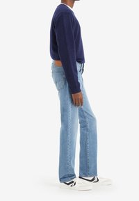 Suéter azul marino, vaqueros azul claro y zapatillas blancas con detalles en negro. El suéter tiene un escote en V, los vaqueros tienen un corte recto.