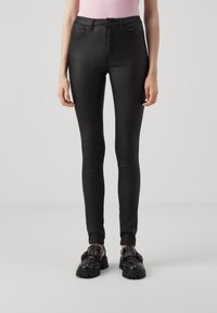 Jeans skinny noirs taille haute avec une texture lisse, un design à cinq poches et des détails de couture subtils, associés à des chaussures noires chunky.