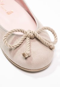 Lys beige ruskinds balletflade med en rund tå og en dekorativ snor-dukke. Indvendigt har den en blød rosa foring. Glat struktur overalt.