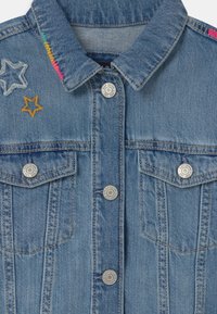 Blå denimjacka med två bröstfickor, silverfärgade tryckknappar och färgglad stjärnbroderi på kragen och axlarna.