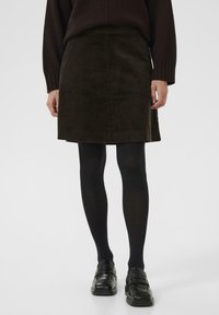 Jupe en velours côtelé marron avec une coupe droite, au-dessus du genou, associée à des collants noirs et des mocassins noirs, présentant une texture subtile et des rayures.