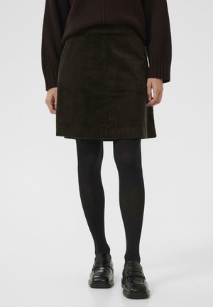Jupe en velours côtelé marron avec une coupe droite, au-dessus du genou, associée à des collants noirs et des mocassins noirs, présentant une texture subtile et des rayures.