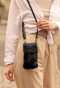 Borsa a tracolla nera in pelle con una texture liscia, forma rettangolare e chiusura a flap; presenta hardware dorato e cinturini regolabili.