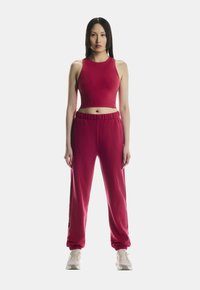 Punane sportlik lühikesed top ja sobivad dressipüksid, millel on elastne v�öökoht ja mansetid, sujuva tekstuuri ja minimalistliku disainiga.