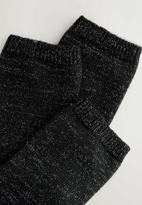 Juodos megztos kojų šilomos su tekstūruota raštu ir metaliniais siūlais. Guma viršuje užtikrina tvirtą prigludimą. Minkšta ir lanksti medžiaga.