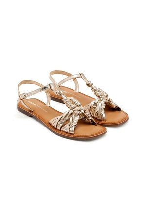 Sandalias planas con un diseño trenzado metálico dorado y suela marrón. Cuentan con una correa ajustable en el tobillo y punta abierta.