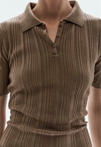 Polo marron à côtes avec des manches courtes et un col, comportant une patte de boutonnage à trois boutons et un motif de tissu texturé.