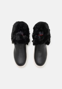 Svarta läder slip-on skor med krage av konstpäls. Vit gummisula. Mjuk textur med synlig branding inuti.