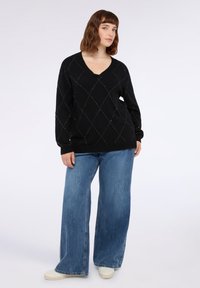 Zwarte v-hals trui met een ruitpatroon en zilveren accenten, gecombineerd met wijde blauwe jeans en lichtgekleurde sneakers.