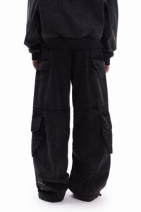 Črne kavbojske hlače s sproščenim krojem, z več žepi in zakovicami na robu, ki ustvarjajo teksturiran, robusten videz.
