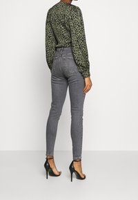 Top de manga larga con estampado de leopardo verde, jeans ajustados gris de cintura alta, tacones de aguja negros, tejido suave, diseño ajustado y detalles sutiles.