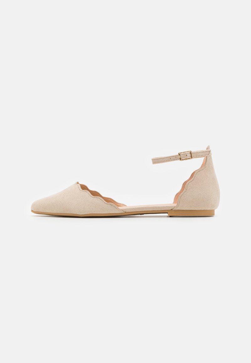 Chaussure plate beige avec bords festonnés, bout pointu, bride à la cheville et boucle sur un fond clair.
