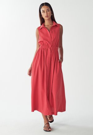 Sleeveless coral dress with button-down front, cinched waist, and side pockets. Length reaches mid-calf, made from lightweight fabric.