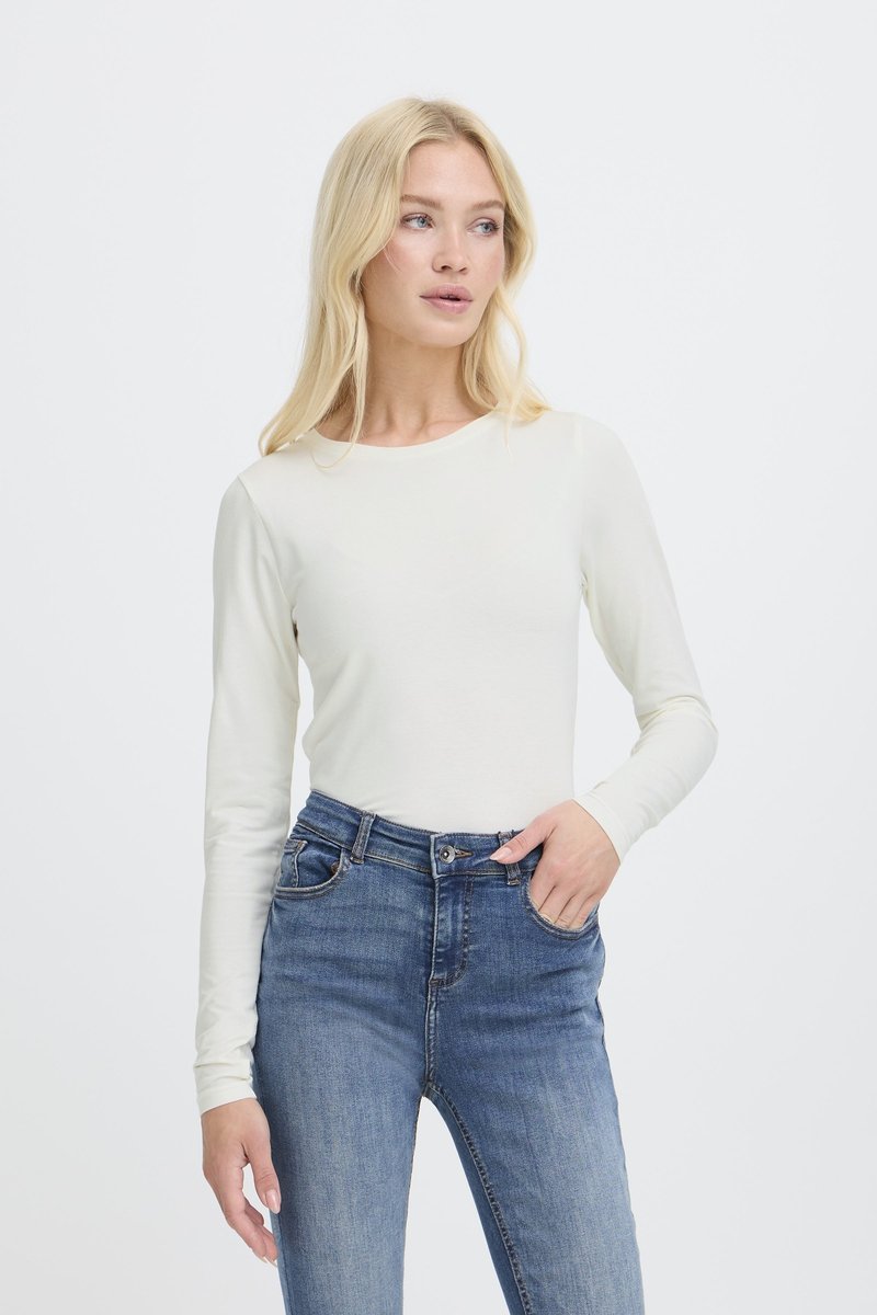 Haut à manches longues, crème clair, en tissu lisse, associé à un jean denim bleu ajusté avec une taille mi-haute et des coutures classiques.