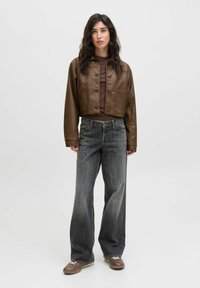 Giubbotto cropped in pelle marrone con chiusura a bottoni e tasche frontali, abbinato a jeans grigi scuri e larghi e scarpe marroni. Design semplice.