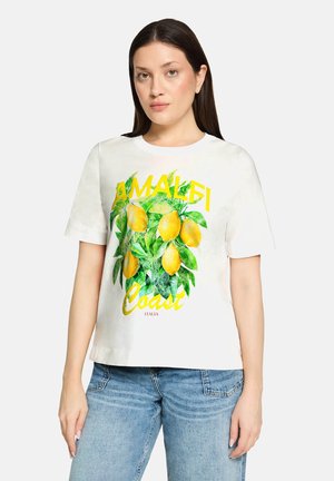 Kvinde iført hvid T-shirt med gule citroner og grønne blade og teksten "Amalfi Coast Italia", kombineret med blå jeans.