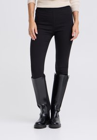 Fekete testhez simuló leggings, térdig  érő, fényes fekete bőrből készült csizmával, mely hasítékkal és oldalsó kampókkal rendelkezik a méretállításhoz.