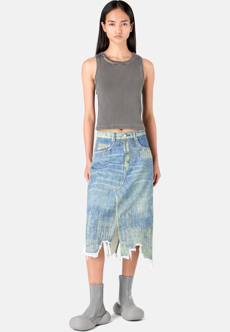 Canottiera grigia a costine abbinata a una gonna midi in denim blu sbiadito con orlo strappato e spacco frontale; modello che indossa stivali alla caviglia grigi con zip.