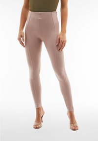 Leggings beige aderenti con vita alta, realizzati in tessuto liscio, caratterizzati da dettagli di cucitura discreti e una zip laterale.