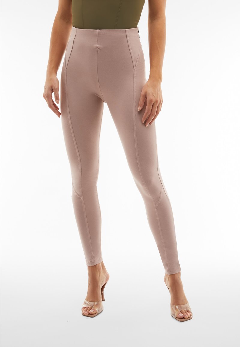 Leggings beige aderenti con vita alta, realizzati in tessuto liscio, caratterizzati da dettagli di cucitura discreti e una zip laterale.