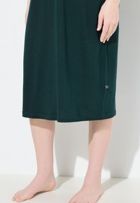 Abito al ginocchio di un verde scuro realizzato in tessuto morbido. Design semplice con forma dritta, caratterizzato da un piccolo dettaglio con logo vicino all'orlo.