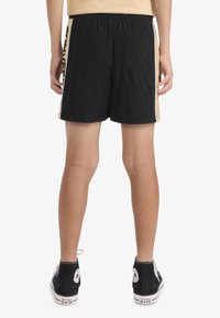 Shorts noirs avec une taille élastique, dotés d'une bande latérale jaune et d'une poche arrière. Assortis à des baskets montantes noires.