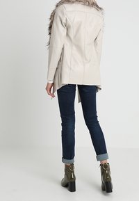 Abrigo de cuero beige claro con cuello de piel, diseño ajustado, costuras en la parte posterior, combinado con jeans de mezclilla oscura y botines olive con tacón grueso.
