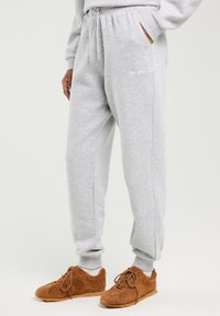 Osoba nosząca jasno szare spodnie dresowe z elastycznym pasem i ściągaczami, białe skarpetki oraz brązowe zamszowe trampki na sznurowadła.