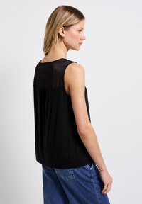 Černý top bez rukávů s texturovaným síťovaným zadním dílem a volným střihem. Tkanina je měkká, s volně drapovaným designem a mírným skládáním.