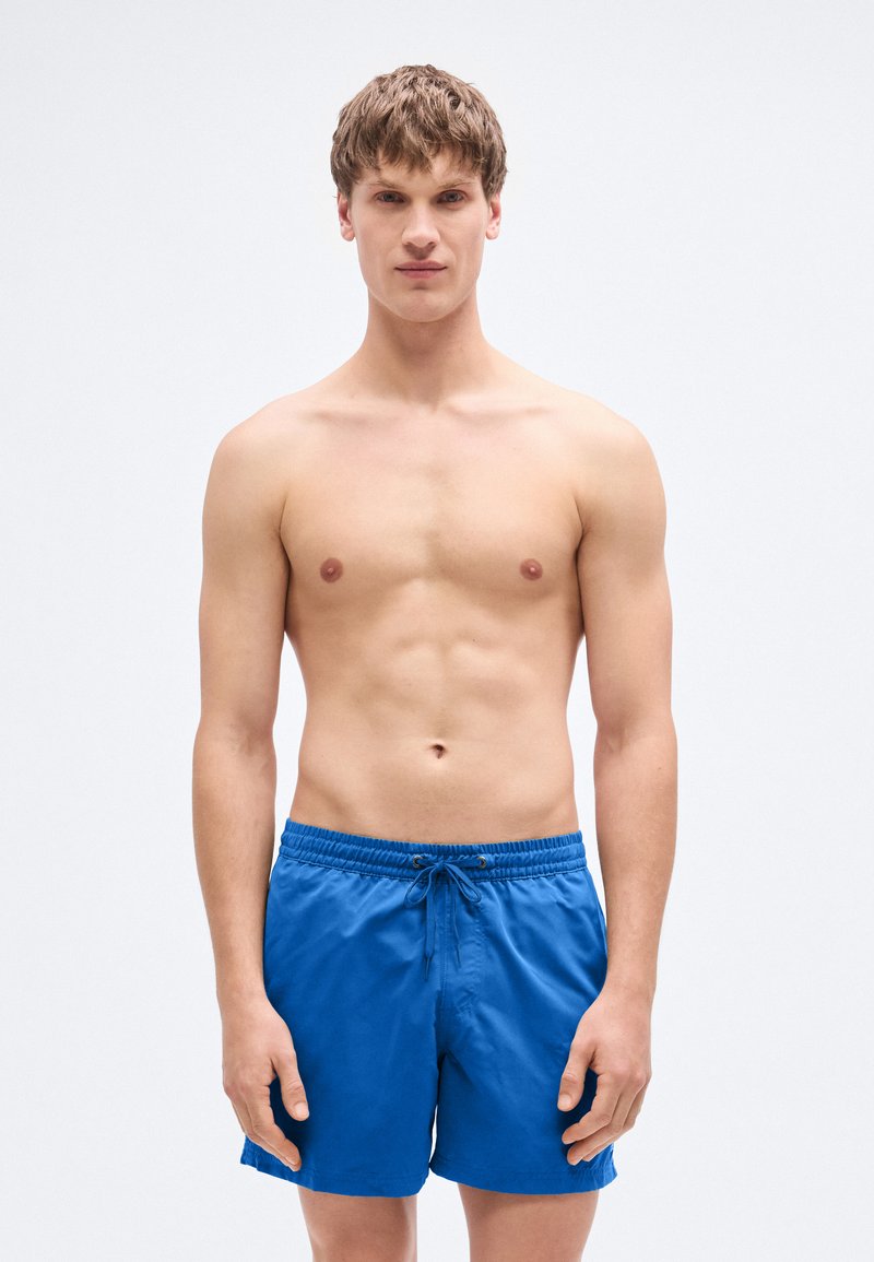 Μπλε μαγιό σορτς από ελαφρύ ύφασμα. Διαθέτει ελαστική μέση με κορδόνι, πλαϊνές τσέπες και κομμένο πάνω από το γόνατο.