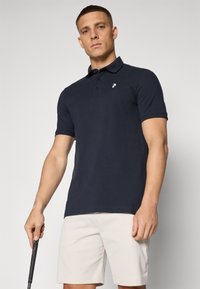 Námornícky polo tričko s golierovým dizajnom, krátkymi rukávmi a malým bielym logom na ľavej hrudi, skombinované s svetlo béžovými šortkami.