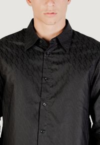 Camicia nera con bottoni, caratterizzata da un motivo testurizzato, colletto classico, bottoni neri e una finitura liscia.