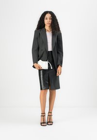 Blazer nero a righe sottili su top rosa chiaro, abbinato a una gonna a matita in pelle nera con spacco frontale. Tenne una pochette bianca.
