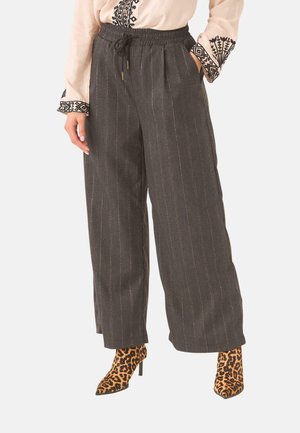 Mujer vistiendo pantalones anchos de rayas finas oscuras, blusa beige bordada y botines de tacón alto con estampado de leopardo.