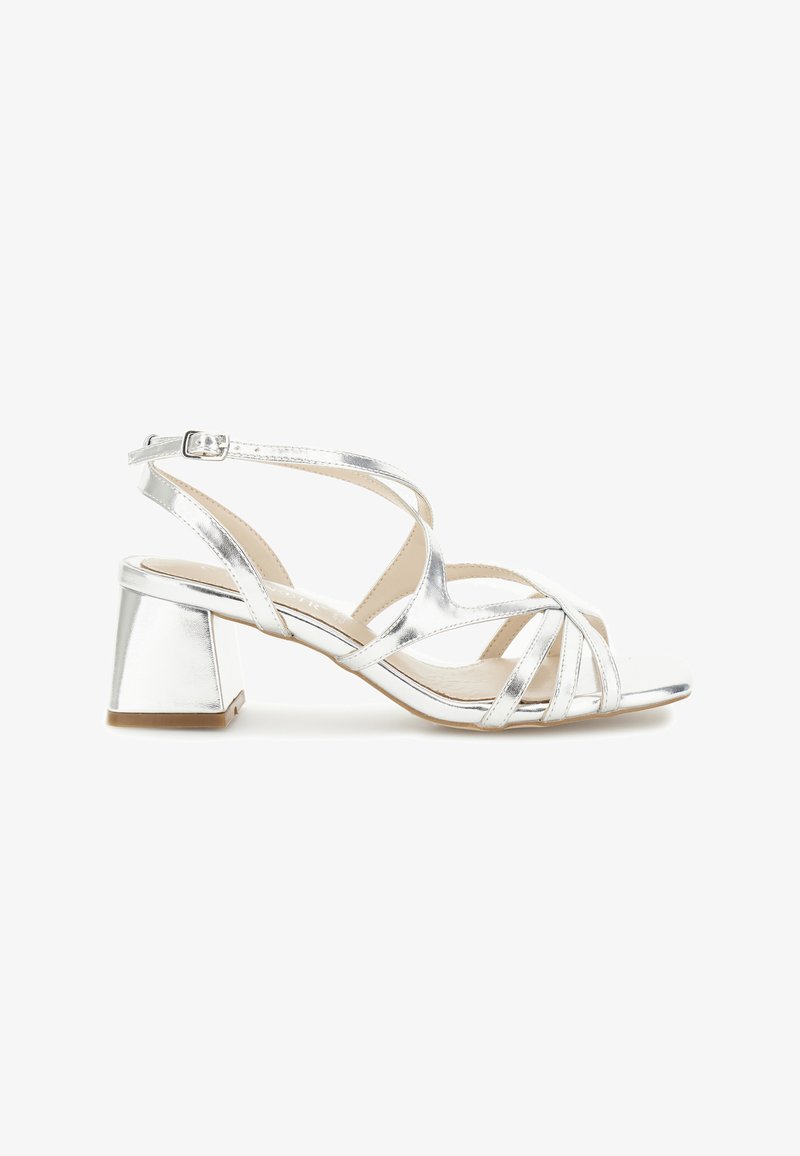 Sandale métallique argentée à talon bloc, dotée de brides croisées, design à bout ouvert et sangle réglable à la cheville. Texture lisse.