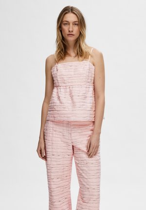 Ensemble deux pièces texturé rose comprenant un haut sans manches à design superposé et un pantalon ample avec une texture similaire.