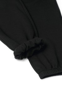 Czarne dresowe spodnie z fleecem w środku, z elastycznymi mankietami, z jednym mankietem złożonym, aby pokazać miękką podszewkę.