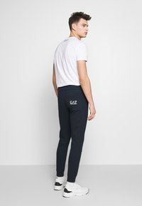 Jūras spēku jogger bikses ar elastīgām gumijām, mīksts audums un aizmugurējā kabata ar baltu EA7 logo. Saskaņotas ar baltu apkakles T-kreklu.