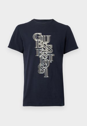 Tamsiai mėlynas trumpomis rankovėmis marškinėlis su vertikaliu baltu užrašu "GUESS EST. 1981" sluoksniuotu šriftu priekyje.