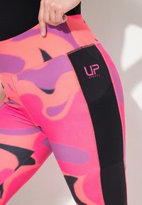Rosa och lila mönstrade leggings med svarta accenter, utrustade med en sidficka och logotypen "UP SPORTS" i rosa på den svarta delen.